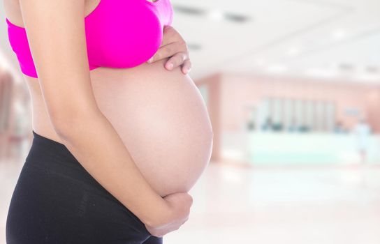 Close-up of pregnant woman belly with her hand on it in hospital background