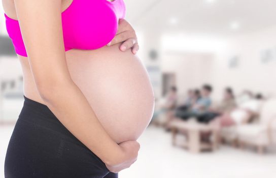 Close-up of pregnant woman belly with her hand on it in hospital background