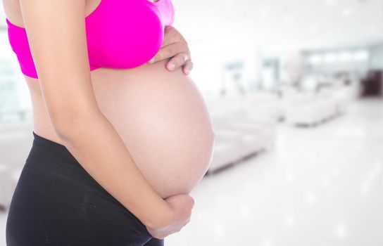 Close-up of pregnant woman belly with her hand on it in hospital background