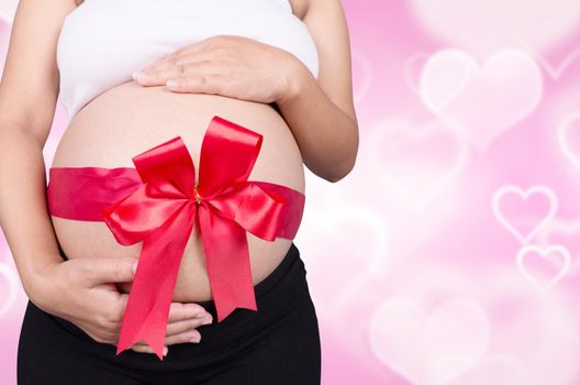 close up pregnant woman with red ribbon gift on belly on heart backrground