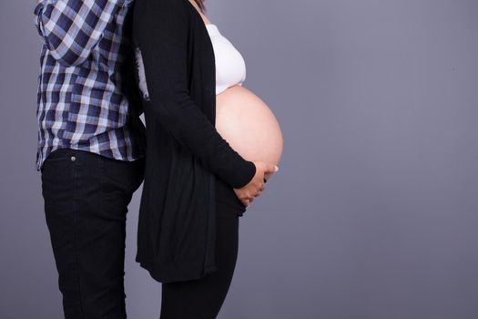 Pregnant woman with her husband on gray wall background