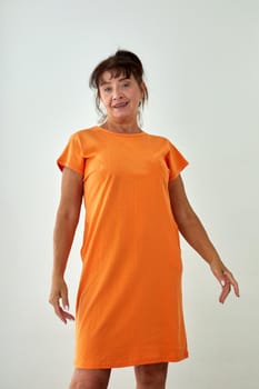 Middle age female model in casual orange dress looking at camera against white background