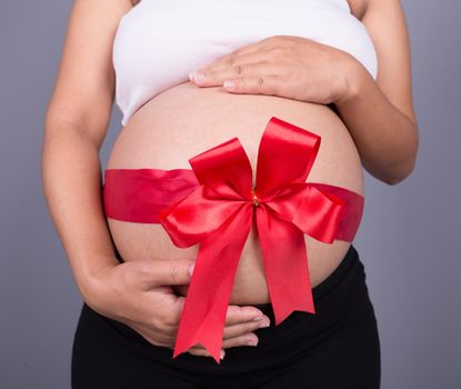 close up pregnant woman with red ribbon gift on belly