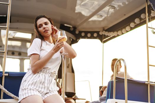 Young woman holding a wineglass and sitting on deck of sailing yacht boat
