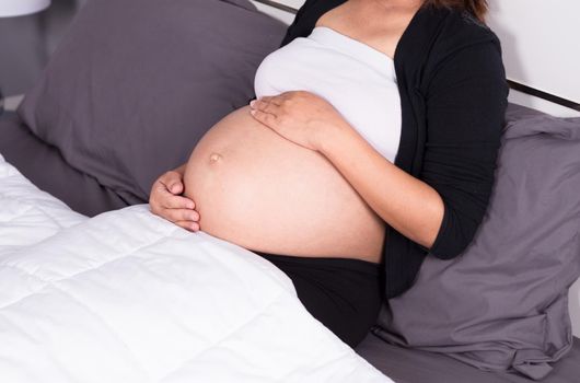 close up belly of pregnant woman sitting on bed in the bedroom at home