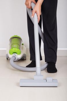 woman legs with vacuum cleaner cleaning floor at home