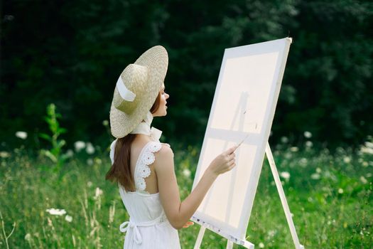 Woman in white dress in nature paints a picture of a landscape hobby. High quality photo