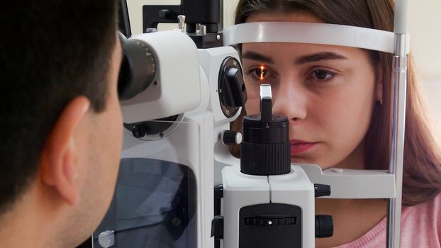 Ophthalmology treatment - a young woman with pink lips checking her visual acuity - pupil reaction to light. Mid shot