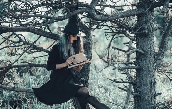 Young witch reading a magic book in autumn forest. Halloween theme