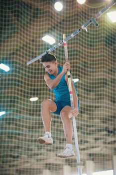 Pole vaulting indoors - young fit smiling man jumping leaning on the pole. Mid shot