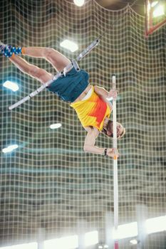 Pole vaulting indoors - a sportive man jumping over the bar - leaning on the pole. Mid shot