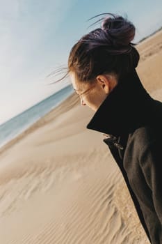 Young woman wearing in coat walking on sand beach and looking at sea