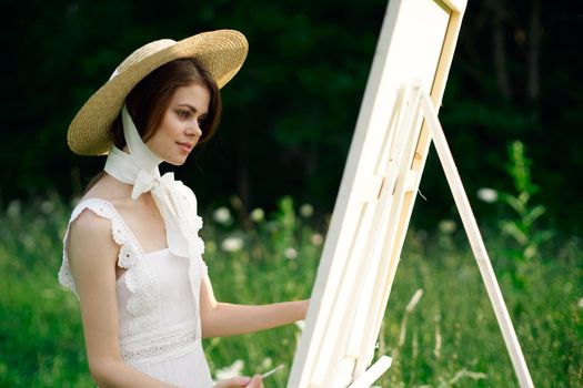 Woman in white dress paints a picture on nature easel. High quality photo