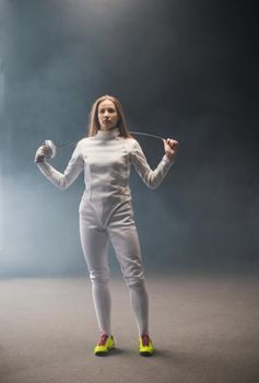 A young woman fencer standing in the studio with a sword behind her shoulders - her long hair is down. Mid shot