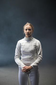 A young woman fencer with her hair in a bun standing with a sword down. Mid shot