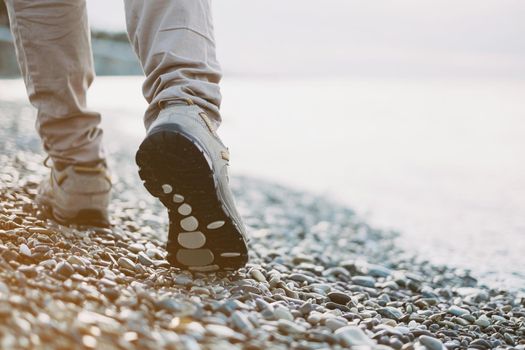 View of female legs walking on pebble coast near the sea