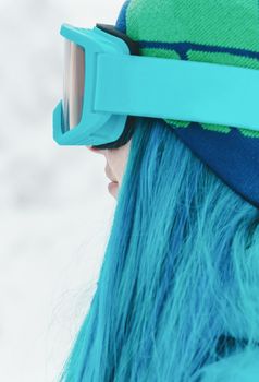 Young woman snowboarder with blue hair in protective sunglasses outdoor, close-up portrait