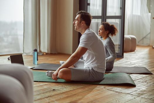 Sporty couple is sitting on mats in front of notebook and doing training together during quarantine