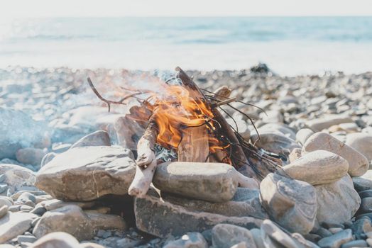 Bonfire on pebble coast on background of sea, no people