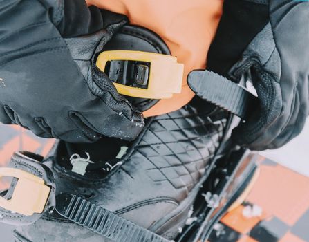 Rider putting on her snowboard and tightening the straps on background of snow in winter, close-up image