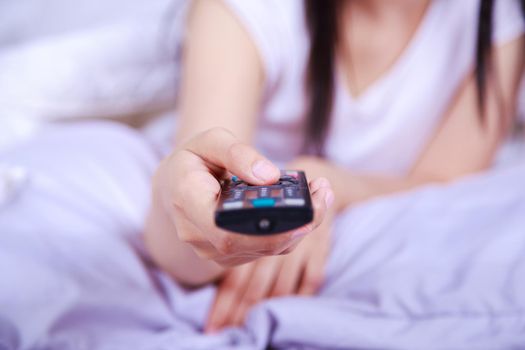 close up tv remote control on hand of woman on the bed