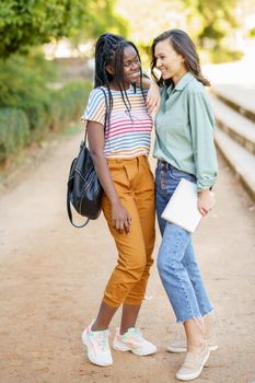 Two multiethnic girls posing together with colorful casual clothing outdoors.