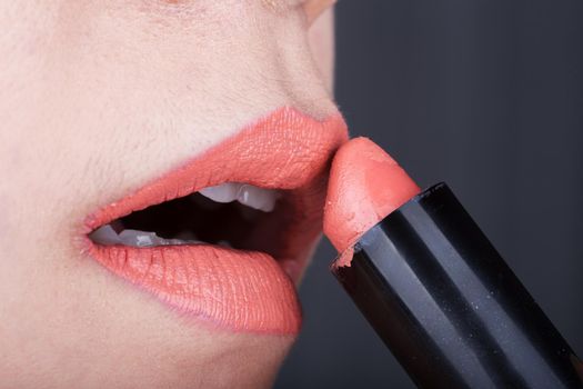 close-up woman applying orange lipstick on her lips