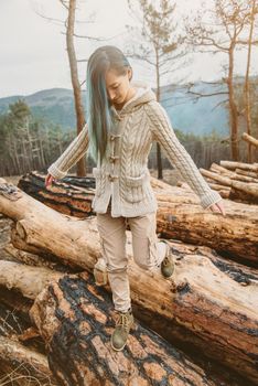 Young woman walking on stack of felled tree trunks in the forest