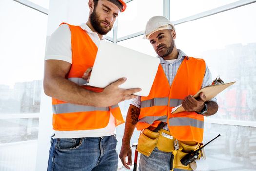 Two specialists supervisors in hardhats using laptop at construction site for work, close up