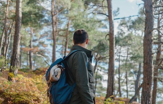 Unrecognizable traveler young man with backpack walking in autumn forest