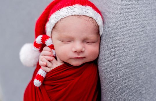 Charming newborn in red hat sleeping with knitted christmas cane candy