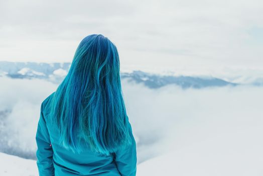 Unrecognizable young woman with blue hair looking at mountains in winter, rear view