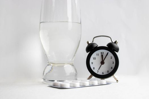 Medical tablets and a glass of water next to the clock on a white background.