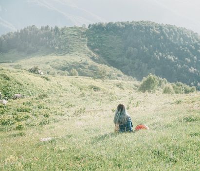 Young woman is resting on summer mountain meadow in sunny day, rear view.