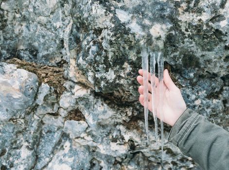 Female hand holding icicles on stone wall