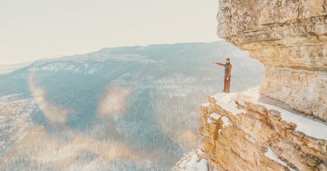 Explorer young man standing on high cliff Eagle shelf and pointing into the distance in winter, Mezmay, Russia. Image with sunlight effect.