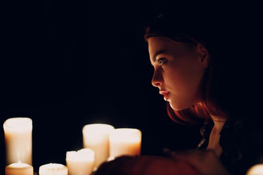 Young woman profile portrait with candles light in darkness. Edge lit face