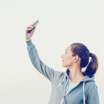 Fitness woman doing selfie with smartphone and listening music in headphones outdoor