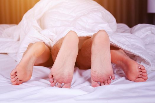 couple feet seen from under blanket on a bed