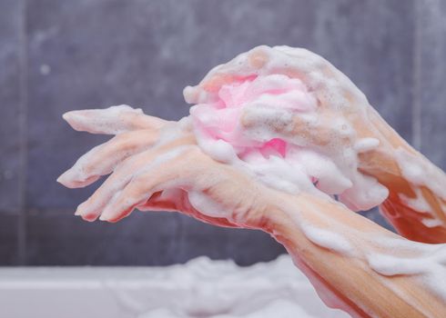 close up of woman washing hand with pink sponge in bathtub in the bathroom