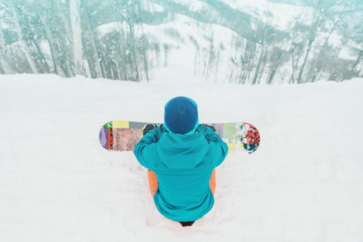 Young woman snowboarder looking at slope among trees in winter on ski resort, rear view