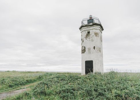 Old lighthouse on summer meadow on high coastline.