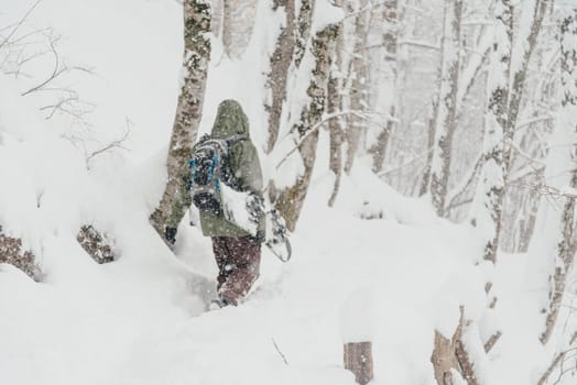 Unrecognizable freerider young man with snowboard walking in winter forest, rear view. Focus on foreground, blurred figure of a man.