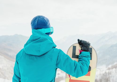 Young woman with snowboard looking at snowy mountains, rear view