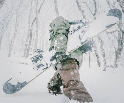 Unrecognizable freerider young man with snowboard walking in winter forest among snowdrifts, close-up