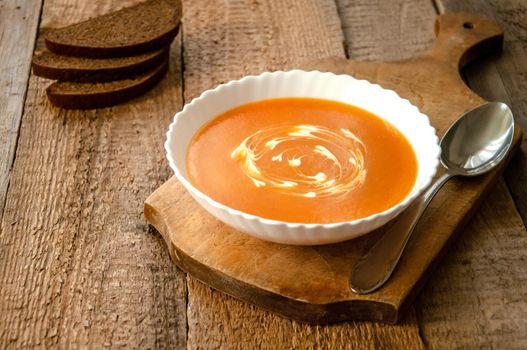 Pumpkin Cream Soup in White Bowl with Bread on Rustic Wooden Background. Autumn Vegetarian Food.