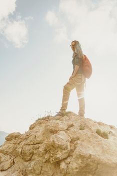 Beautiful hiker girl standing on rocky stone at sunny summer day.