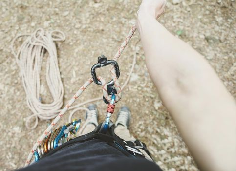 Unrecognizable female climber wearing in safety harness standing with figure eight and rope, point of view.