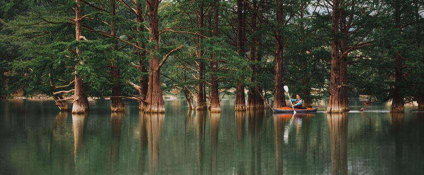 Explorer young man kayaking on lake on background of beautiful cypresses in summer, Anapa, Russia.