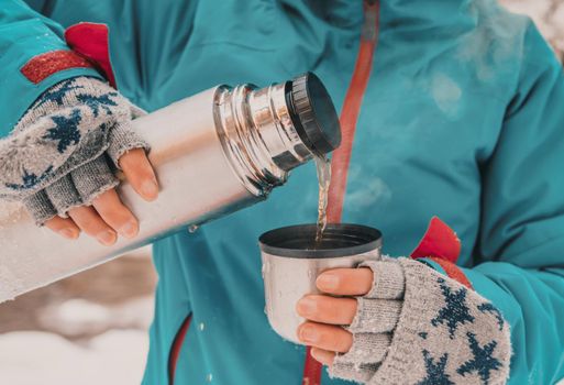 Unrecognizable young woman pouring tea from thermos to cup in winter outdoor, front view